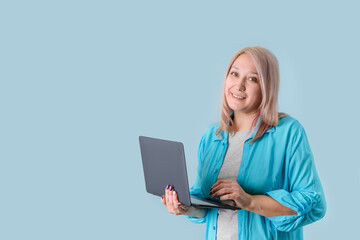 A beautiful blonde woman 35-40 years old holds a laptop in her hands standing on a blue background, copyspace