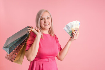 A 40-year-old adult woman with shopping bags and a fan of euro bills in her hand on a pink background, copyspace