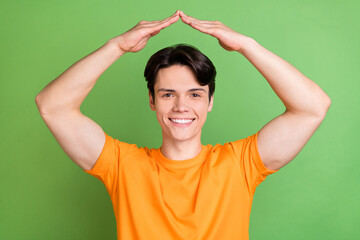 Photo of positive happy young man hold hands above head roof house isolated on green color background