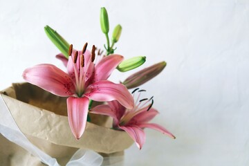 Bouquet of fresh pink lilies, a package with flowers on a light background with a place for an inscription, the concept of a romantic congratulation, invitation, wedding, postcard, Valentine's day
