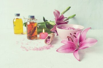 Pink lilies, burning candles, sea salt, oil and tincture of medicinal plants on the table, spa, useful and aromatic cosmetics for care and relaxation
