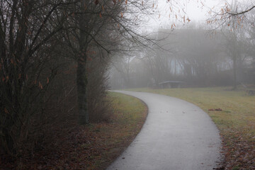 Footpath in a residential area at fog leads to a playground with table tennis table and playground equipment