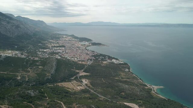 Drone view of a mountain road in the Makarska Riviera region in Croatia, with stunning Adriatic coasts and the town of Makarska in the background.