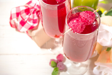 Red mimosas cocktail for Valentine's. Classic mimosa drink with raspberry juice, raspberry and mint decor. With gift box for Valentine day, rose flowers, champagne bottle