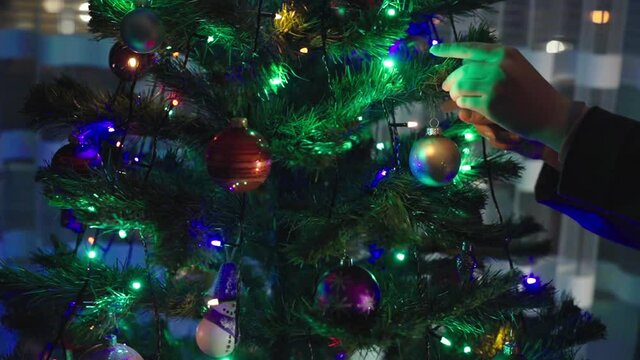 Slow Motion: Young Caucasian Girls Hands Put Christmas Decorations on New Year Tree. Colorful lights shining on tree.