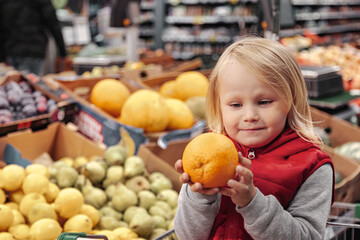 Fototapeta na wymiar Little girl sitting in shopping cart in food fruit store or supermarket