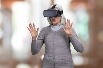 Stunned senior woman with virtual reality headset on abstract bokeh background.