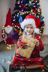 A girl in a hat of santa claus sorts out gifts against the background of a Christmas tree