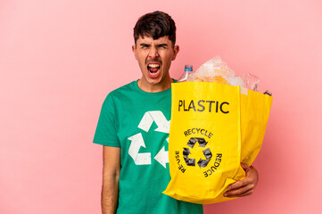 Young mixed race man recycled plastic isolated on pink background screaming very angry and aggressive.