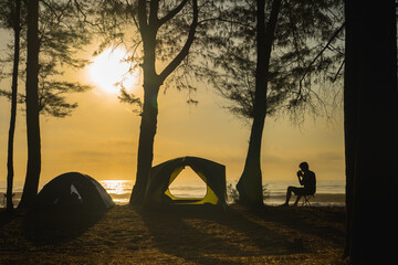 silhouette camping tent with people relax on beach with sunrise and sea background