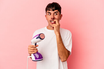 Young mixed race man holding an iron isolated on pink background relaxed thinking about something looking at a copy space.