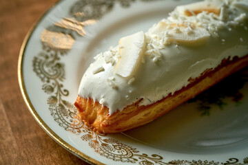 Coconut eclair with white frosting in a white plate on a wooden background