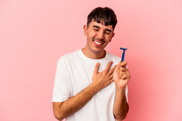 Young mixed race man holding razor blade isolated on pink background laughing and having fun.