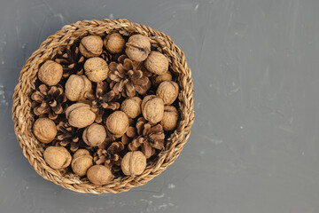 Raw walnuts in shell and pine cones in basket as fall or Christmas table decoration on dark gray background. Top view, copy space