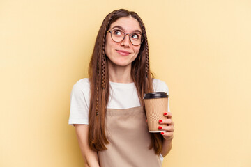 Restaurant waiter woman holding a take away coffee isolated on yellow background dreaming of achieving goals and purposes