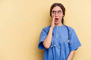 Young nurse caucasian woman isolated on yellow background is saying a secret hot braking news and...