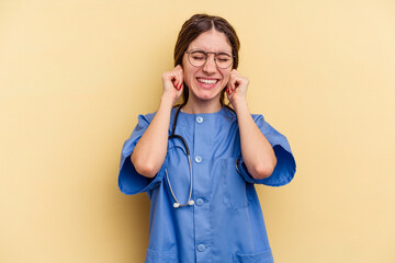 Young nurse caucasian woman isolated on yellow background covering ears with hands.