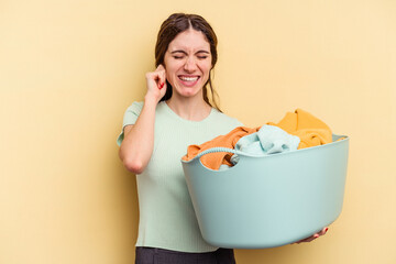 Young caucasian woman holding a clothes basket isolated on yellow background covering ears with...