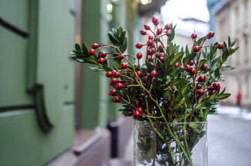 Hawthorn red berries and myrtle greens in a vase on a rainy street background with lights.