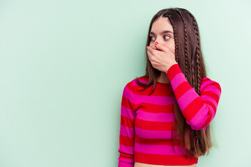 Young caucasian woman isolated on green background thoughtful looking to a copy space covering mouth with hand.