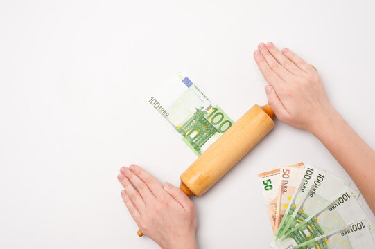 Images on the topic of world economics and finance. Allegory of financial cuisine. The rolling pin and chef's hands roll out the bill of one hundred euro. Top view.