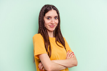 Young caucasian woman isolated on green background who feels confident, crossing arms with determination.