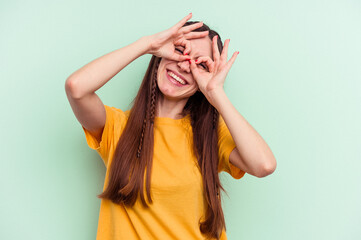 Young caucasian woman isolated on green background showing okay sign over eyes