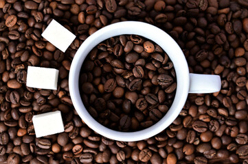 white cup with coffee beans on a coffee background. Three pieces of sugar next to the cup. Close-up. Flat layout with top view