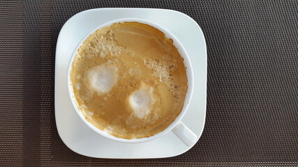 White cup with coffee on a brown background. Brewed coffee with froth