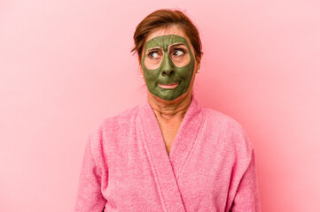 Middle age caucasian woman wearing a facial mask isolated on pink background confused, feels doubtful and unsure.