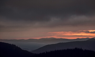 Disturbing sunrise in the mountains. Magnificent view of the clouds illuminated by the rising sun.