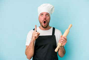 Young baker man isolated on blue background pointing upside with opened mouth.