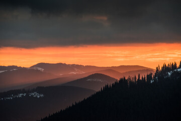 Disturbing sunrise in the mountains. Magnificent view of the clouds illuminated by the rising sun.