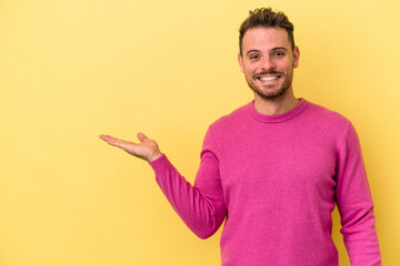 Young caucasian man isolated on yellow background showing a copy space on a palm and holding...