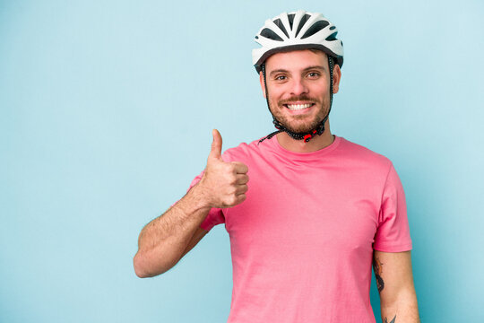 Young caucasian man with bike helmet isolated on blue background smiling and raising thumb up