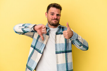 Young caucasian man isolated on yellow background showing thumbs up and thumbs down, difficult...
