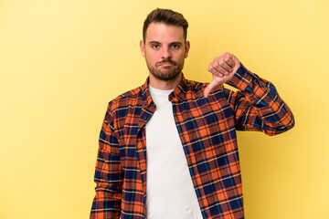 Young caucasian man isolated on yellow background showing a dislike gesture, thumbs down....