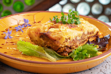 lasagna on an orange plate accompanied by lettuce leaves, watercress and purple flowers.