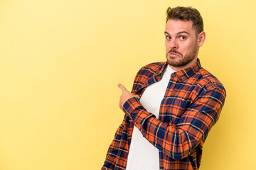 Young caucasian man isolated on yellow background smiling and pointing aside, showing something at blank space.