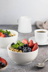 Breakfast with granola, berries and freshly brewed coffee on gray background, side view, vertical composition