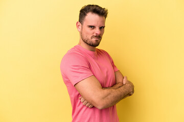 Young caucasian man isolated on yellow background frowning face in displeasure, keeps arms folded.