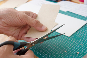 Men's hands are cutting craft cardboard with scissors. Production of handmade jewelry, notebooks, applications.