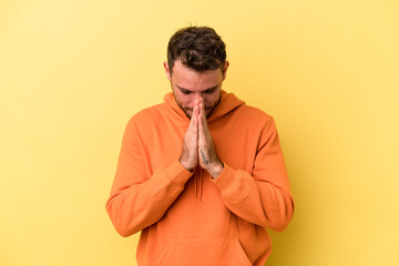 Young caucasian man isolated on yellow background praying, showing devotion, religious person...
