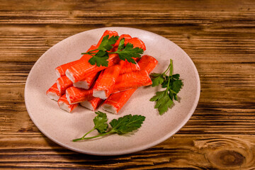Ceramic plate with pile of crab sticks and parsley twig on a wooden table