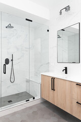 A beautiful luxury, modern bathroom with a light wood cabinet, walk-in shower with marble tiled walls, and black faucets and hardware. - obrazy, fototapety, plakaty