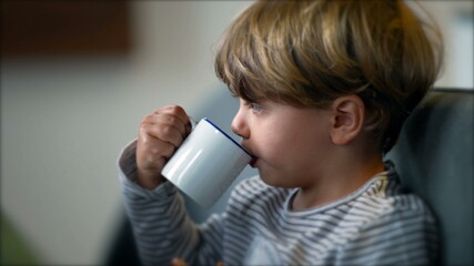 Toddler drinks from mug. Child drinking from cup in morning breakfast.