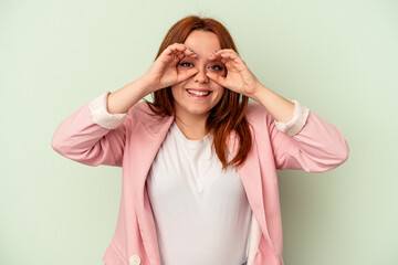 Young caucasian woman isolated on green background showing okay sign over eyes