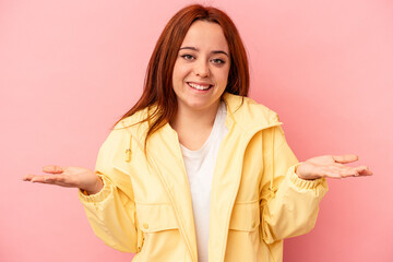 Young caucasian woman isolated on pink background makes scale with arms, feels happy and confident.