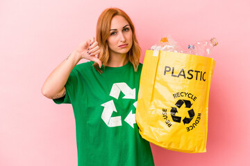 Young caucasian woman recycled plastic isolated on pink background showing a dislike gesture, thumbs down. Disagreement concept.