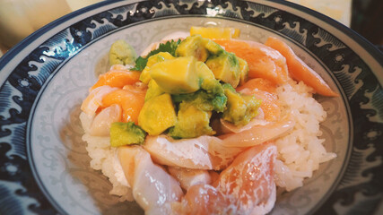 Close up images of japanese seafood rice bowl or kaisendon sashimi donburi or KAISEN CHIRASHI DON which have raw fresh ogura uni shrimp crab and fish on rice bowl. wood table from top view angle.